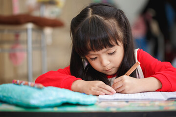 Asian little girl learning and writing in notebook with pencil