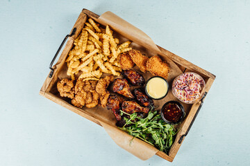 Top view of fried chicken with french fries and sauce on a wooden tray on the table