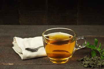 Tulsi or holy basil tea in transparent glass cup with fresh and dry tulsi leaf on wooden background. Ayurvedic medicine in India.