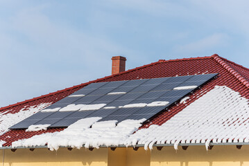 Solar photovoltaic panels PV on a snowy house roof, blue sky with copy space. - 408821549