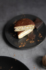 Round chocolate brownie on a black plate and cocoa powder on a gray concrete table. Sweets and coffee background.