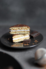 Round chocolate brownie on a black plate and cocoa powder on a gray concrete table. Sweets and coffee background.