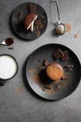 Round chocolate brownie on a black plate and cocoa powder on a gray concrete table. Sweets and coffee background. view from above. flat lay