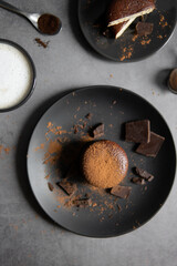 Round chocolate brownie on a black plate and cocoa powder on a gray concrete table. Sweets and coffee background. view from above. flat lay