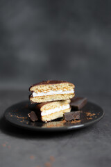 Round chocolate brownie on a black plate and cocoa powder on a gray concrete table. Sweets and coffee background.