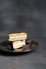 Round chocolate brownie on a black plate and cocoa powder on a gray concrete table. Sweets and coffee background.
