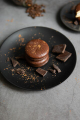 Round chocolate brownie on a black plate and cocoa powder on a gray concrete table. Sweets and coffee background.