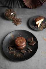 Round chocolate brownie on a black plate and cocoa powder on a gray concrete table. Sweets and coffee background.