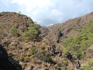 Natural picture of the stone slope of the mountain range illuminated by the sun on a background of white clouds approaching the sky.