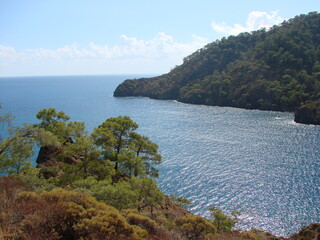 View from the hiking trail to the azure surface of the sea bay that reflects the sun's rays on the forests on the slopes of the surrounding mountains.