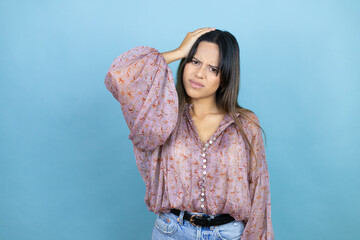 Beautiful latin woman wearing a pink shirt over blue isolated background putting one hand on her...