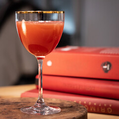 Red cocktail in Nick and Nora glass on wood table with red books in background