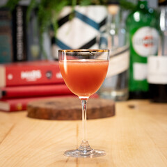 Red cocktail in Nick and Nora glass on wood table with red books in background