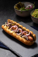 Gourmet dirty hot dog sandwich with various garnish on black slate background. Healthy option of fast food.