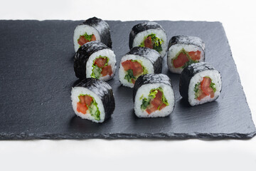 Sushi roll with salmon, avocado and cheese on a black stone plate on a white plate. Sushi menu. Japanese food.