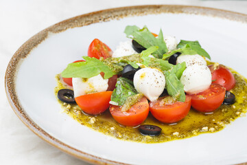 Caprese salad with fresh cherry tomatoes, mini mozzarella, pesto, basil, olive oil and balsamic sauce on a white plate and on a white background Mediterranean diet concept. Italian healthy food.