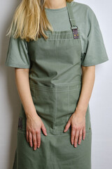 A woman in a kitchen apron. Chef work in the cuisine. Cook in uniform, protection apparel. Job in food service. Professional culinary. Green fabric apron, casual clothing. Handsome baker posing