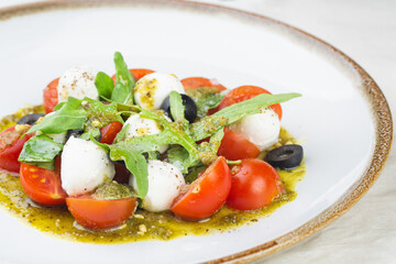 Caprese salad with fresh cherry tomatoes, mini mozzarella, pesto, basil, olive oil and balsamic sauce on a white plate and on a white background Mediterranean diet concept. Italian healthy food.