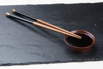 .Black board on a white background. Empty black granite stone rectangular board on white textured background. sushi sticks and soy sauce on coasters on a stone board