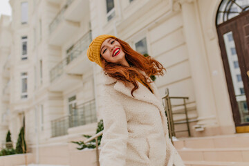 Jocund long-haired girl in hat smiling in cold day. Ginger young woman walking outdoor in winter.