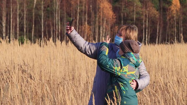 A woman with a boy in masks are photographed together on a smartphone. Walk in the park in autumn. Camping on a hike. Healthy lifestyle concept. At sunset, in the evening, warm soft light.