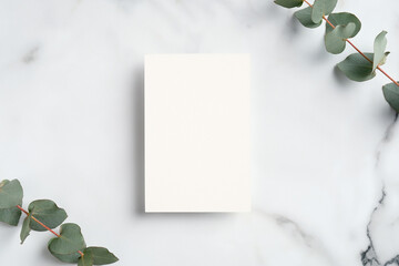 Wedding invitation mockup. Blank paper card and eucalyptus branches on white marble table. Elegant...