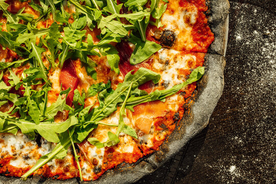 A top view of appetizing pizza with black dough and various vegetables