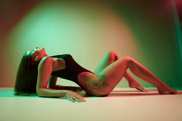 Portrait of a tattoo woman wearing in a black bodysuit lying on the studio floor.