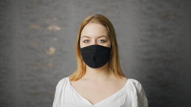 Beautiful young woman with blue eyes wearing black mask and looking at you