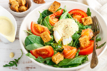 Delicious homemade salad of green leaves (romano, arugula, spinach, lettuce), fresh tomatoes, lightly salted salmon or trout, garlic croutons with poached egg and hollandaise sauce. Selective Focus