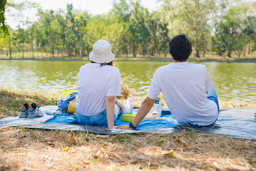 asian couple picnic with happiness feeling in park with lake in springtime