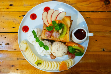 Ice cream on toast with whipped cream, banana slices, strawberry juice and honey in a cup