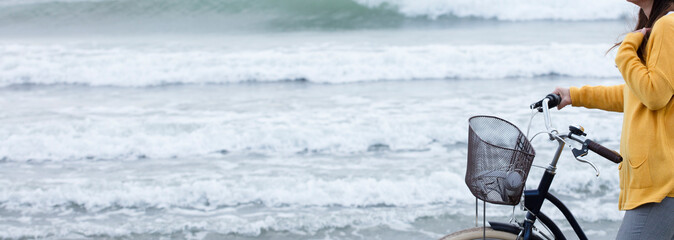 woman with bicycle and yellow sweater, sea with waves in the background, partial view, space for text.