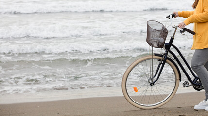 Obraz premium woman with bicycle and yellow sweater, sea with waves in the background, partial view, space for text.