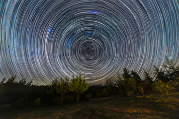 The Earth rotation as seen in the night sky with the star trails. An awe scenery in the outdoors with the forest, the trees and the stars glowing in the distance. A dreamlike and colorful scenery