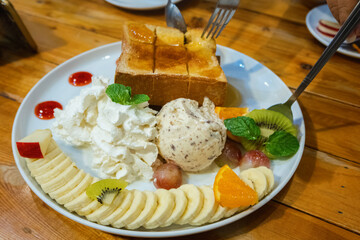 Ice cream on toast with whipped cream, banana slices, strawberry juice and honey in a cup