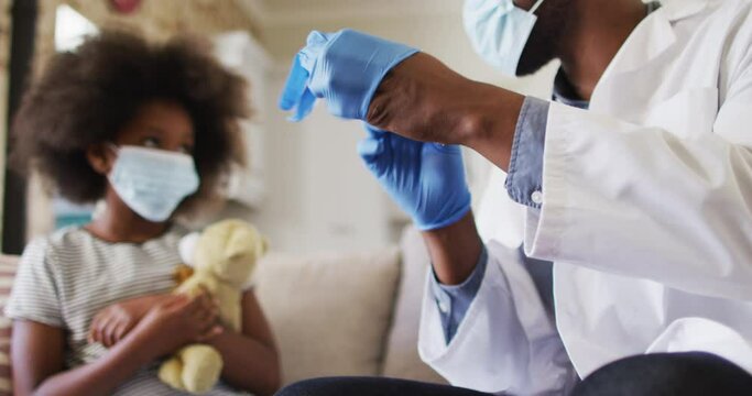 African american doctor in face mask wearing surgical gloves at home