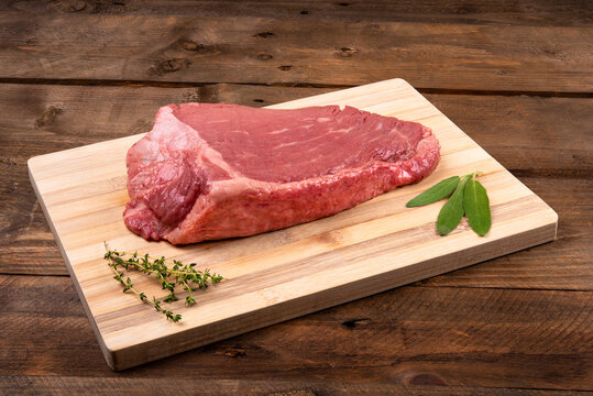 Topside steak on bamboo board with salvia and rosemary on wooden background