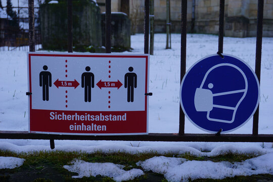 Hinweisschilder zur Beachtung der Corona Ma&szlig;nahmen Sicherheitsabstand einhalten und Mundschutz tragen an einem Zaun angebracht
