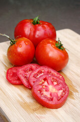 three juicy ripe red wet tomatoes with slices on a light wood background 
