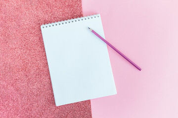 Notebook with blank page and pencil on a pink background.