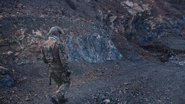 Army soldier with rifle in action in mountains.