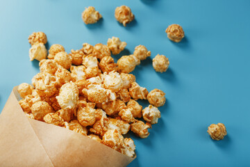 Popcorn in caramel glaze in a paper envelope on a blue background.