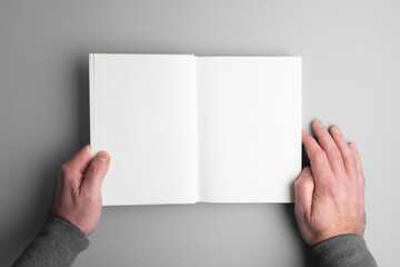overhead view of person opening blank page hardcover book on gray desk surface