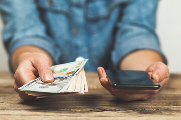 Woman holds dollars and phone in her hands. Online money transfer.