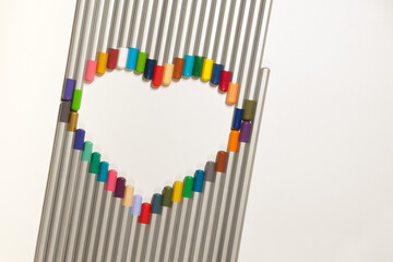 Many colorful pencils folded in the shape of a heart and rays on the white