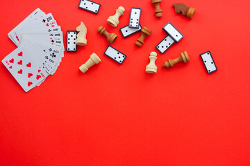Board games on a red background: playing cards, checkers and chess. the view from the top, place under the text