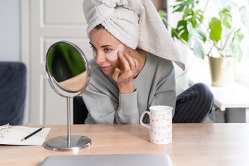 Woman with towel on head applying patches under eyes enriched with collagen, vitamin E, diminishes...
