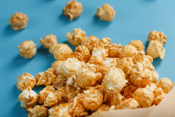 Popcorn in caramel glaze in a paper envelope on a blue background.
