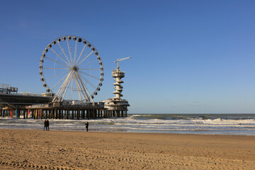 Ferris wheel on De Pier in The Hague Scheveningen on a windy winter day with blue sky and people at the beach, the Netherlands, Europe